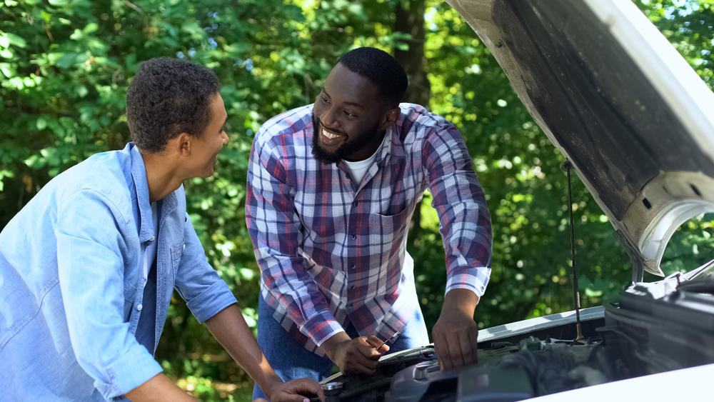 teen talking to adult while looking at car engine