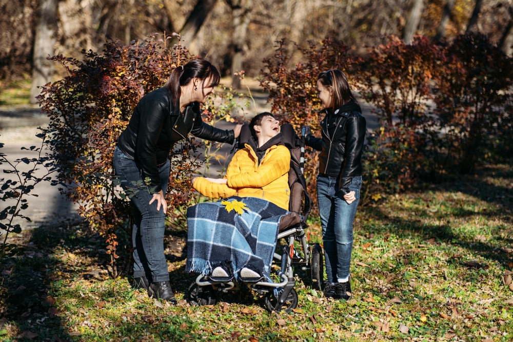 Woman and girl providing laughing on a country roll and stroll with a young man in a wheelchair