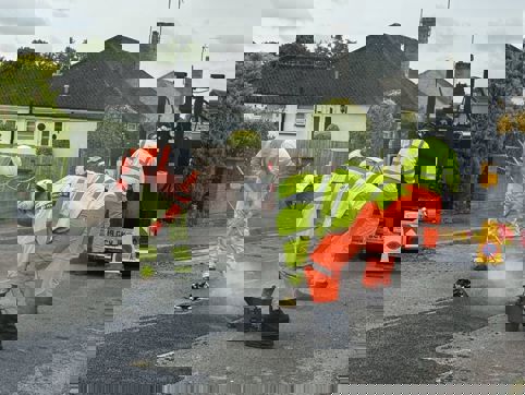 Photo of four people repairing a road with hot asphalt