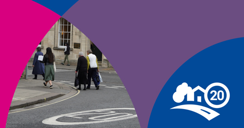 Photo of people walking across a road with a 20 mph sign painted in white
