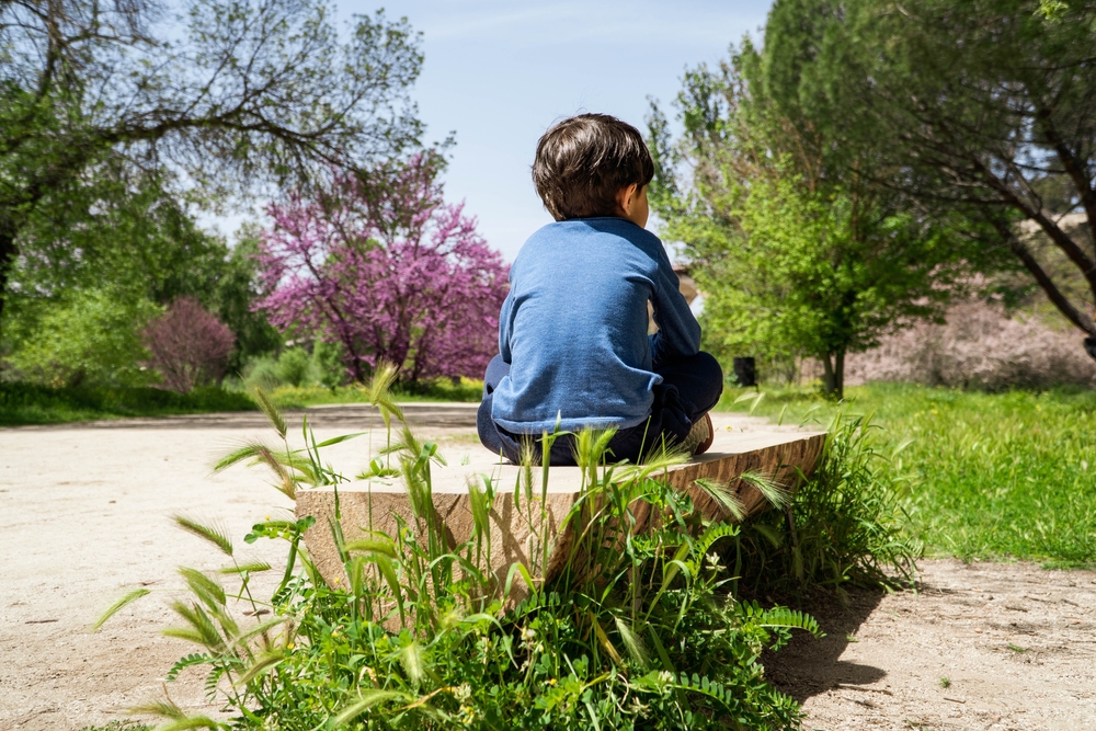 Young person sitting on a path in the sunshine with back to the photographer
