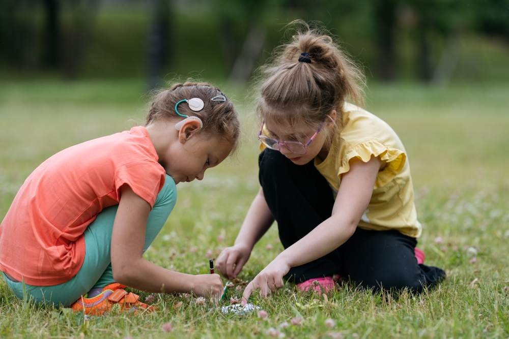 Two girls playing together in park in summer one girl wearing hearing aid