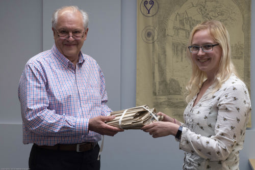 Photograph of two people holding either end of a bundle of documents