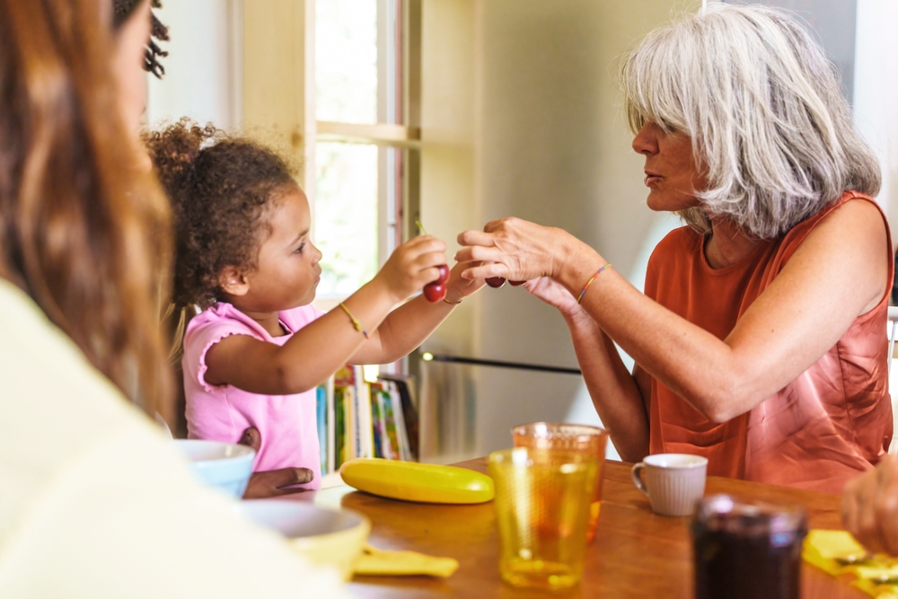 Toddler engages with their grandparent over the breakfast table by bumping knuckles