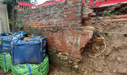 Photo of tall brick wall sagging and supported by heavy bags