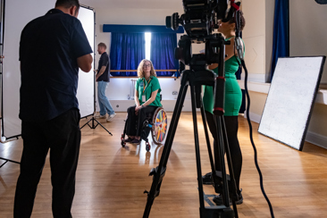 A behind the scenes image showing one a disabled female young actor being filmed in a interview.