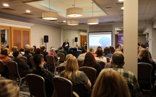 A photograph of Ann James, Gloucestershire County Council’s Director of Children’s Services, delivering a keynote speech to people seated on chairs in a large conference room at the SEND Fair 2026.