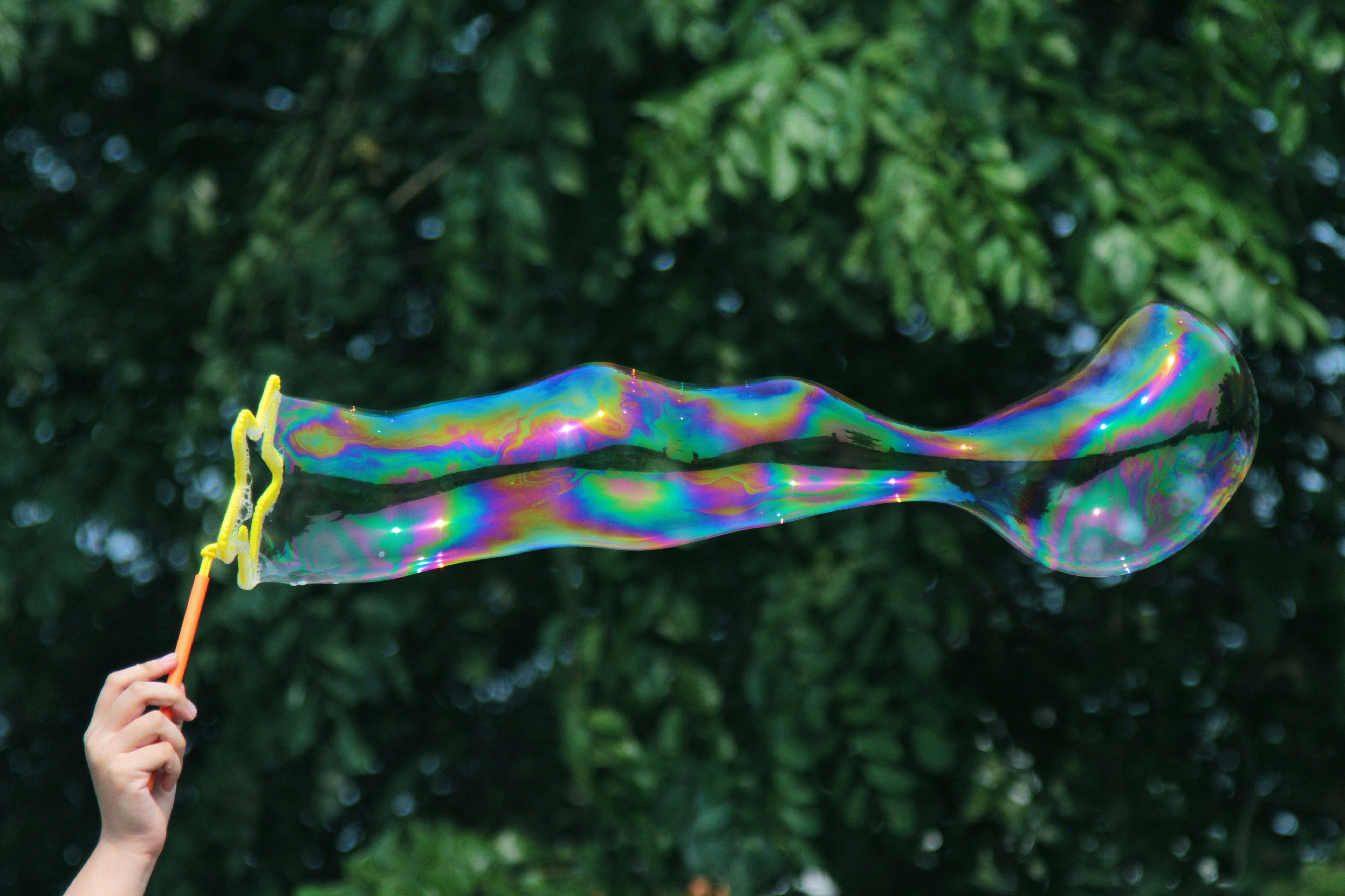 Bubble wand held by child with light refracting across a long horizontal bubble