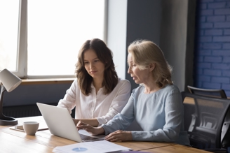 A lady showing a younger girl something on her laptop.