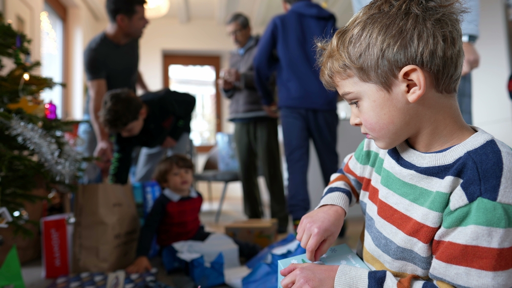 Young boy in striped jumper opening Christmas presents at a distance from others