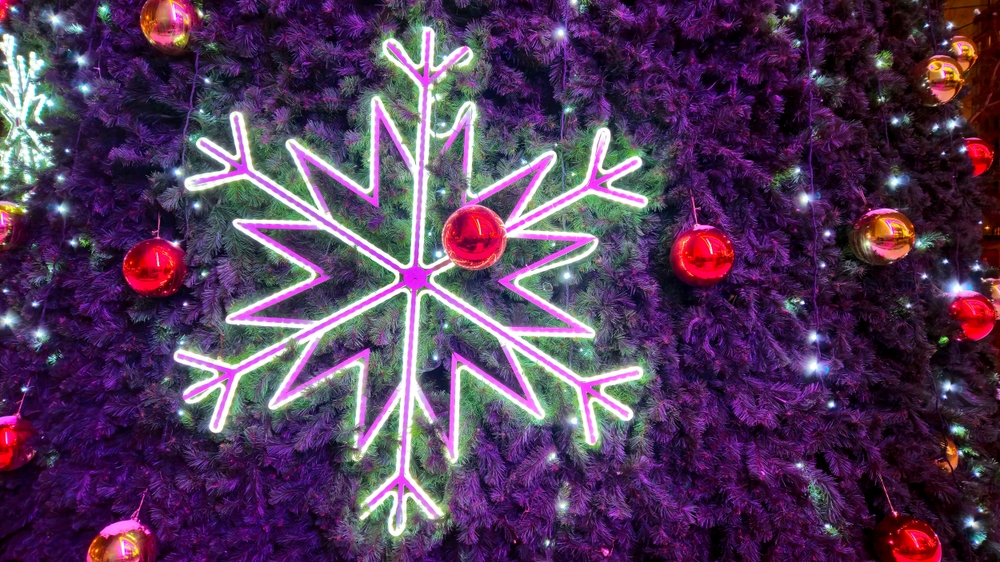 Big glowing snowflake and red glass balls close-up on Christmas tree. 