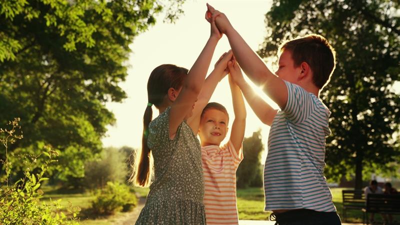 Three children holding their arms up to create a bridge smiling in the Autumn sunshine