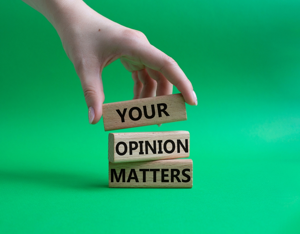 Your opinion matters written on three wooden blocks with a hand placing the blocks on top of each other, with a green background
