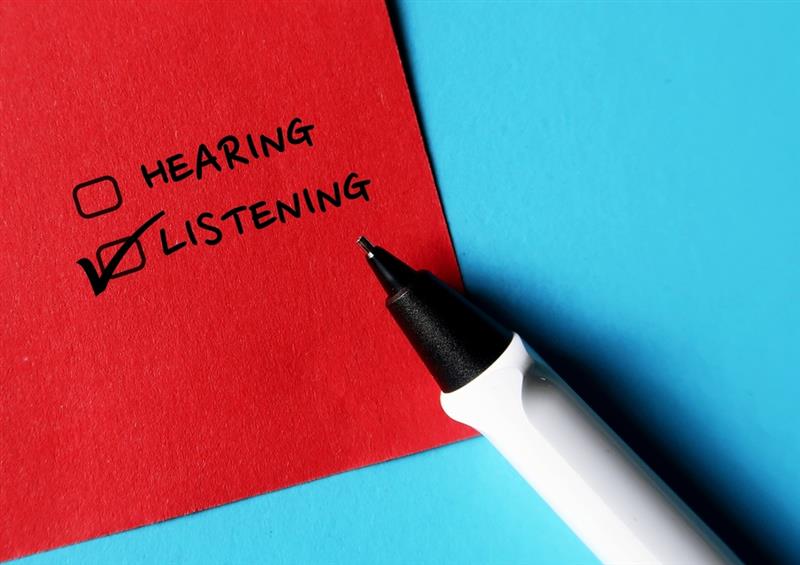 White pen on blue background with red sheet of paper, on it is written hearing and listening with two check boxes and listening is checked