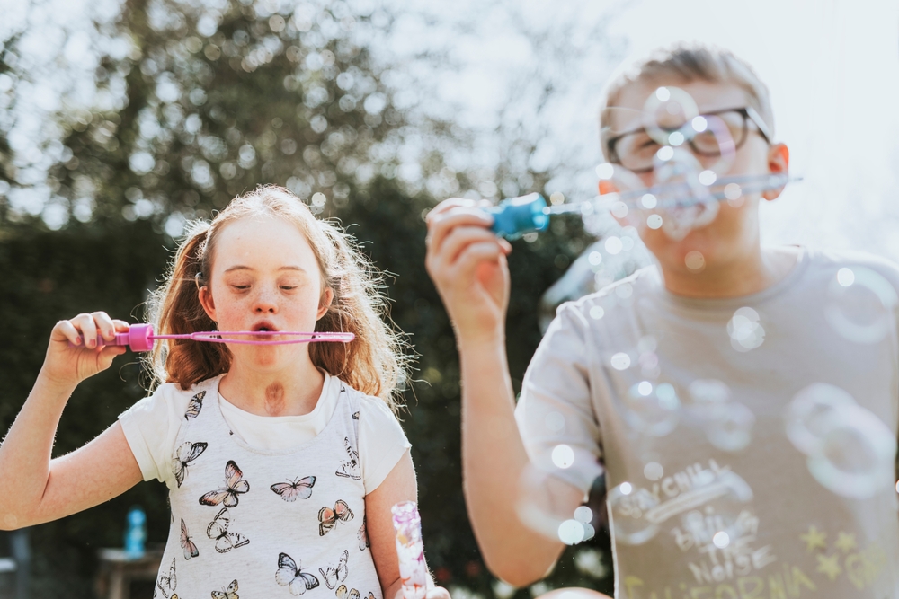 A girl and boy blowing bubbles through bubble wands in a garden
