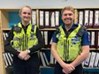 A photo of two police officers, stood in an office.