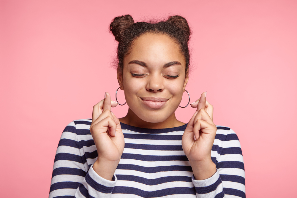 Young person in a stripy top with their eyes closed and fingers crossed