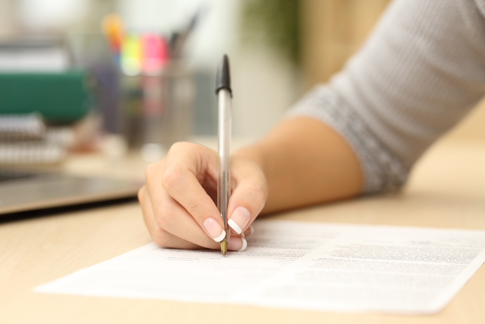 An arm holding a black biro pen writing on a form