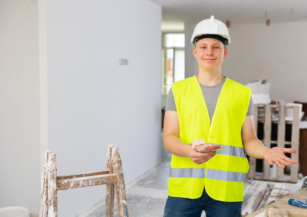 A young man wearing a hi-vis and hard hat, working in the construction sector