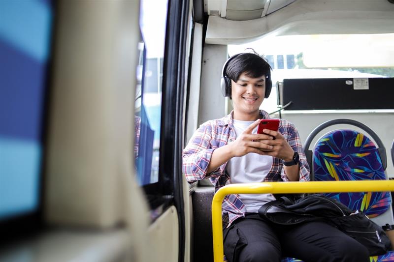 Young man wearing headphones and using mobile phone on the bus.