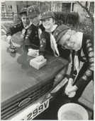 A black and white photo of four young boys cleaning a car