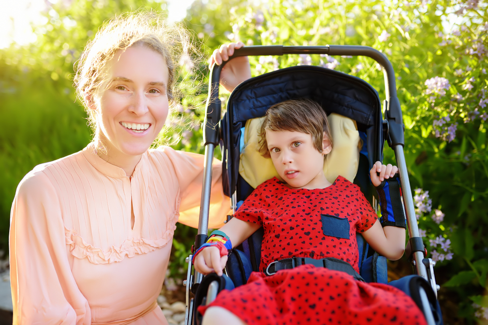A woman smiling holding the handle of a pushchair with a young girl.